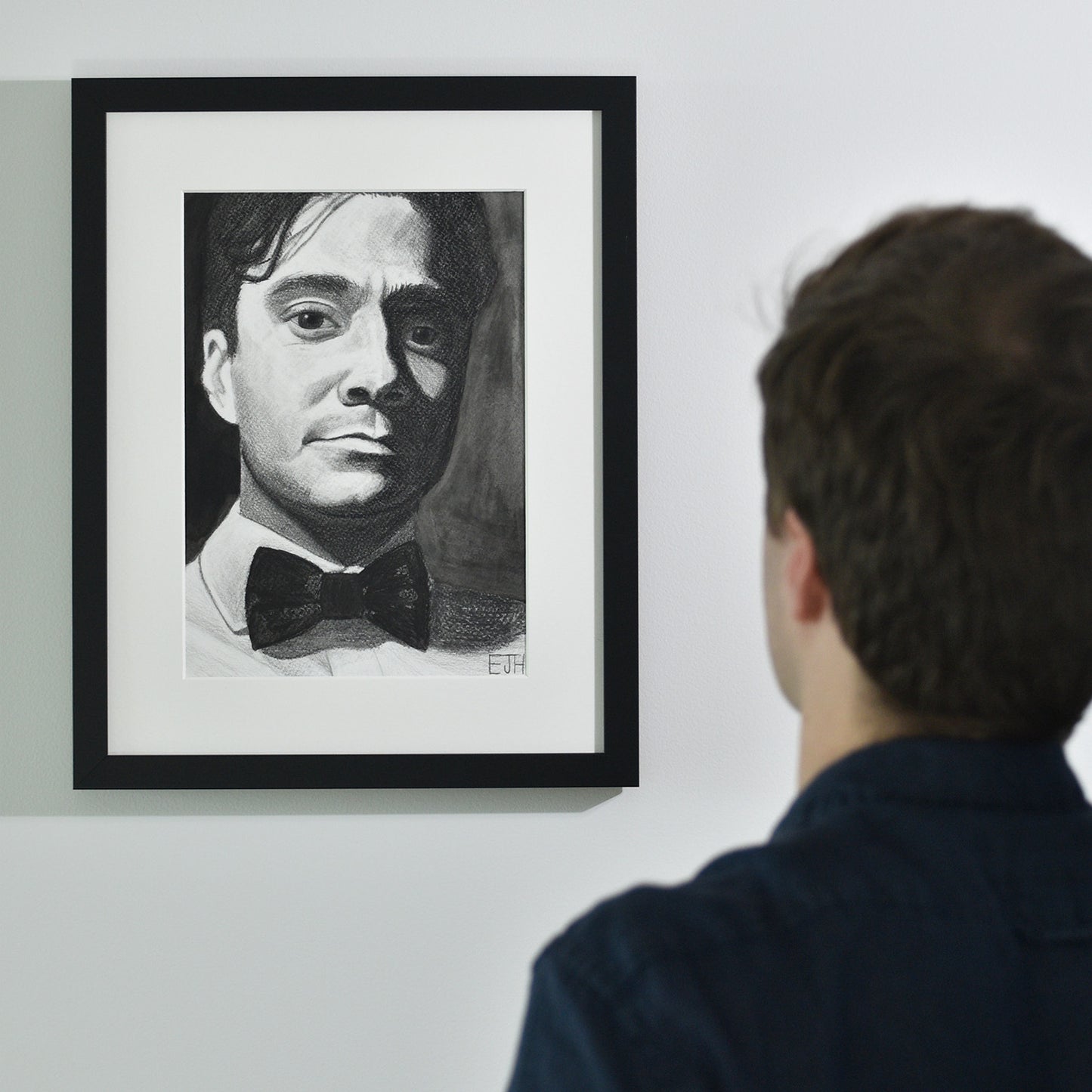 Artist looking at 'Beneath The Surface', framed drawing portrait on a wall.