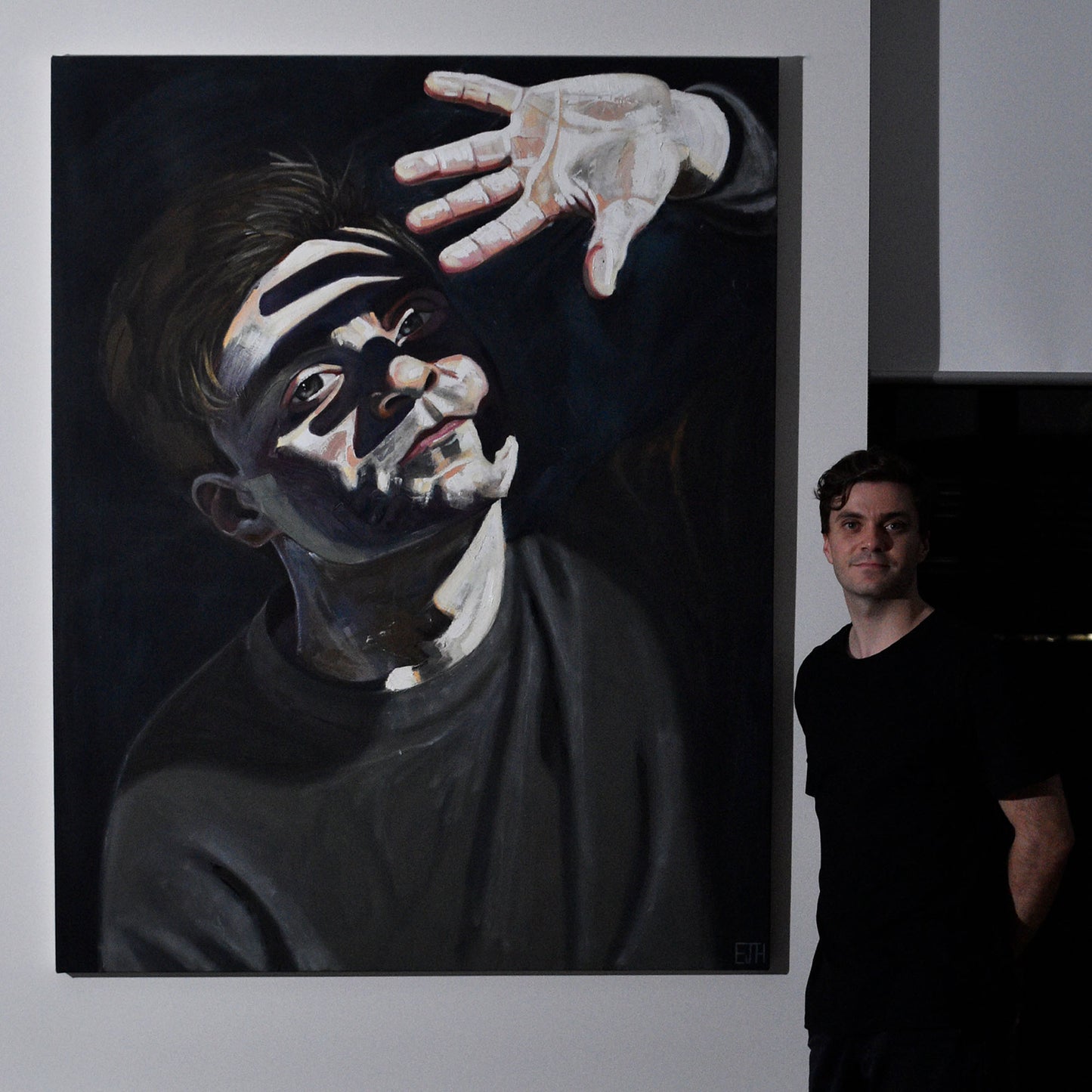 Artist standing next to 'Beyond The Light', a large painting of himself with a bright face and hand.