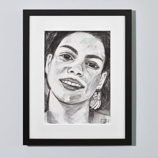 'Charisma' framed portrait drawing of a woman with a smile hanging on a neutral wall in the artist's studio.