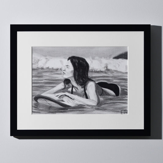 'Soul Surfer' framed portrait drawing of a woman in the ocean hanging on a neutral wall in the artist's studio.