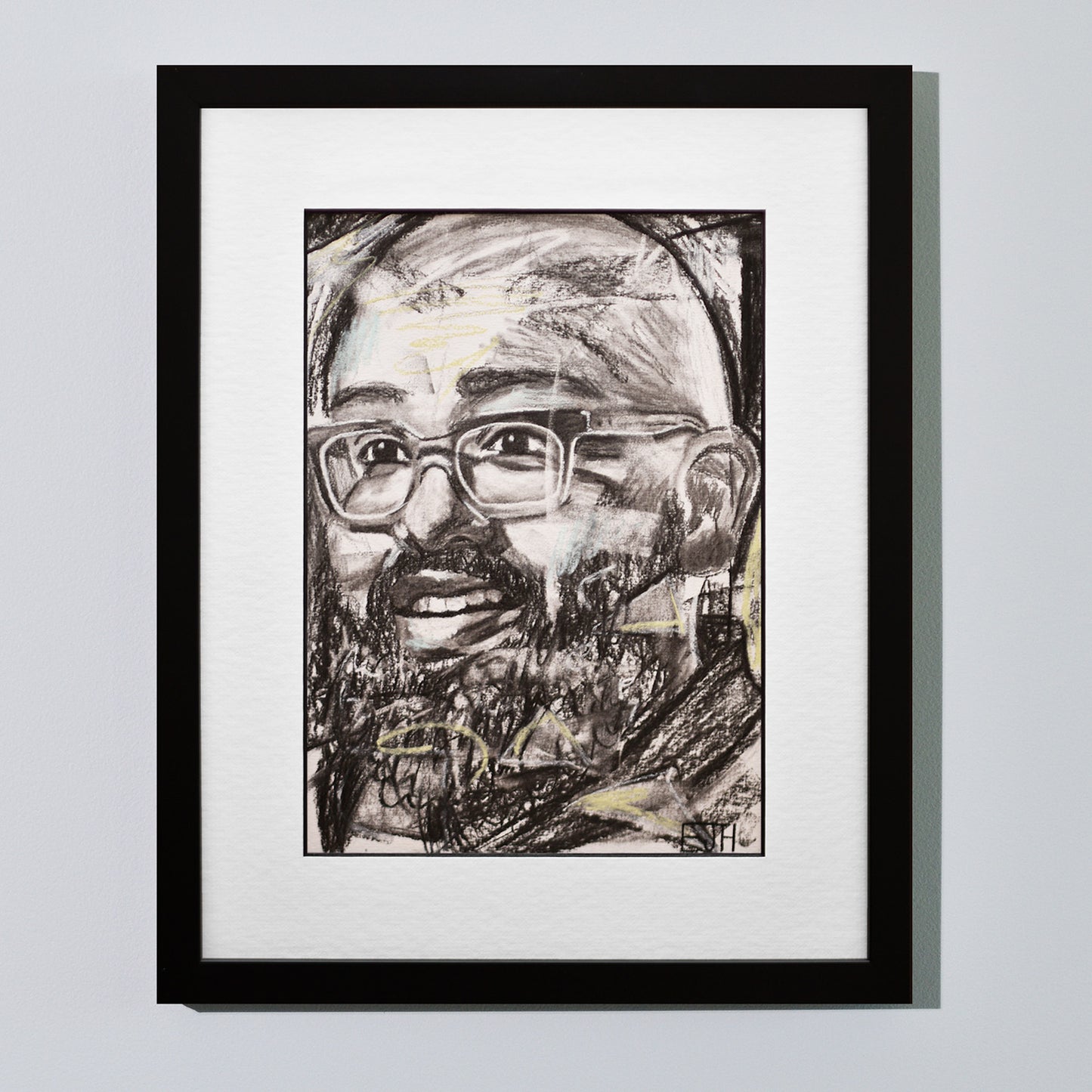 'Amaze' framed portrait drawing of a man with a smile hanging on a neutral wall in the artist's studio.