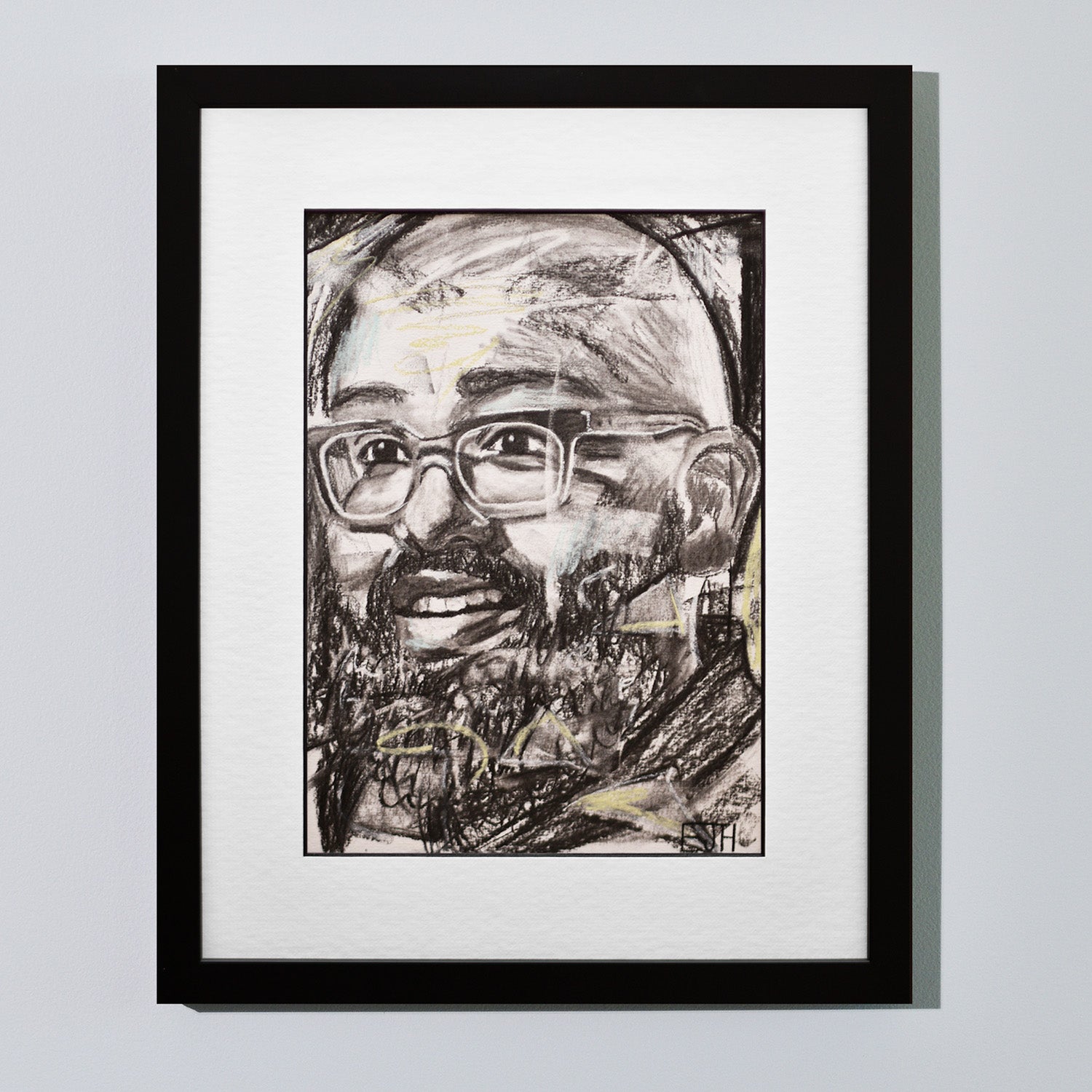 'Amaze' framed portrait drawing of a man with a smile hanging on a neutral wall in the artist's studio.