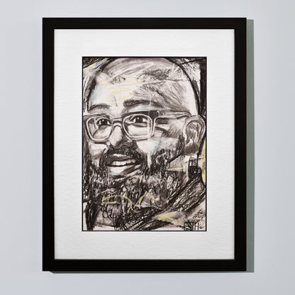 'Amaze' framed portrait drawing of a man with a smile hanging on a neutral wall in the artist's studio.