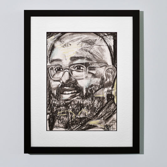 'Amaze' framed portrait drawing of a man with a smile hanging on a neutral wall in the artist's studio.