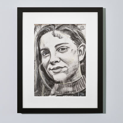 'Believe' framed portrait drawing of a woman with a smile hanging on a neutral wall in the artist's studio.