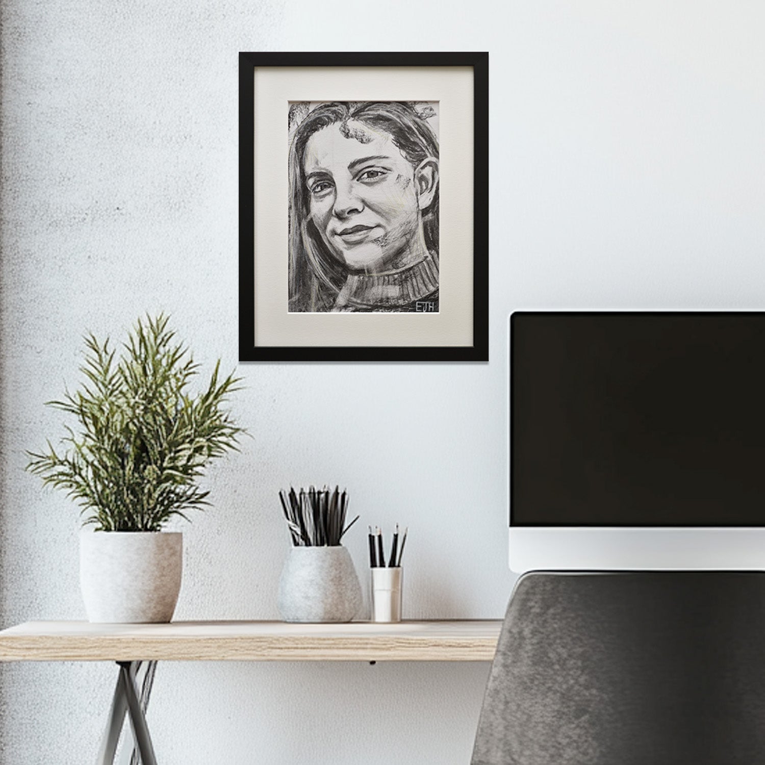 'Believe' framed portrait drawing hanging above a desk with plants and office items.