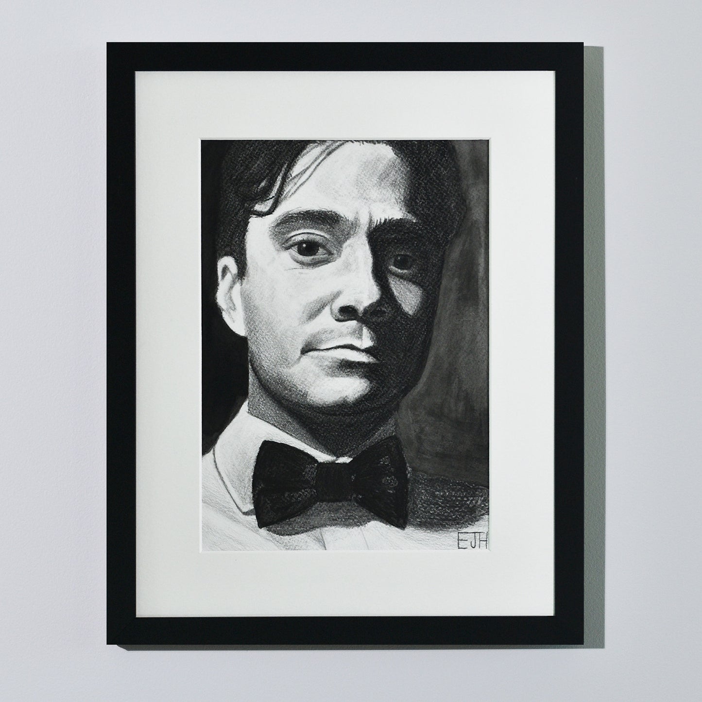 'Beneath The Surface', framed portrait drawing of a man with a bow tie hanging on a neutral wall in the artist's studio.