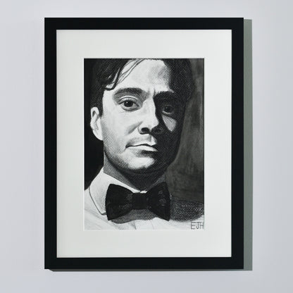 'Beneath The Surface', framed portrait drawing of a man with a bow tie hanging on a neutral wall in the artist's studio.