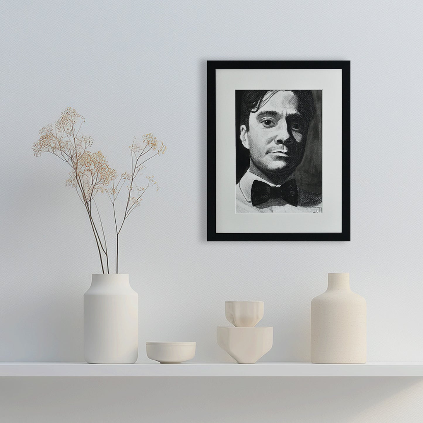 'Beneath The Surface' framed portrait drawing of man with a bowtie hanging on a wall with decorative vases below.