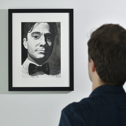 Artist looking at 'Beneath The Surface', framed drawing portrait on a wall.