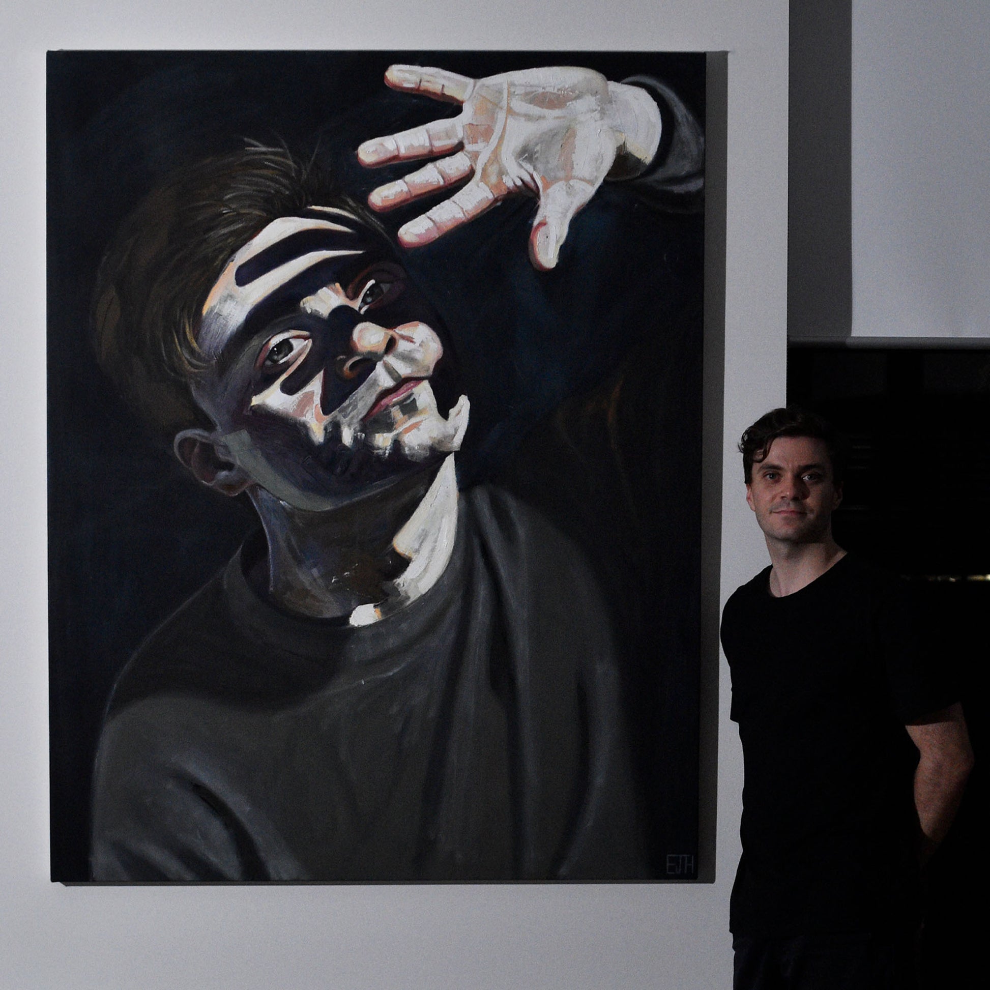 Artist standing next to 'Beyond The Light', a large painting of himself with a bright face and hand.