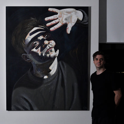 Artist standing next to 'Beyond The Light', a large painting of himself with a bright face and hand.