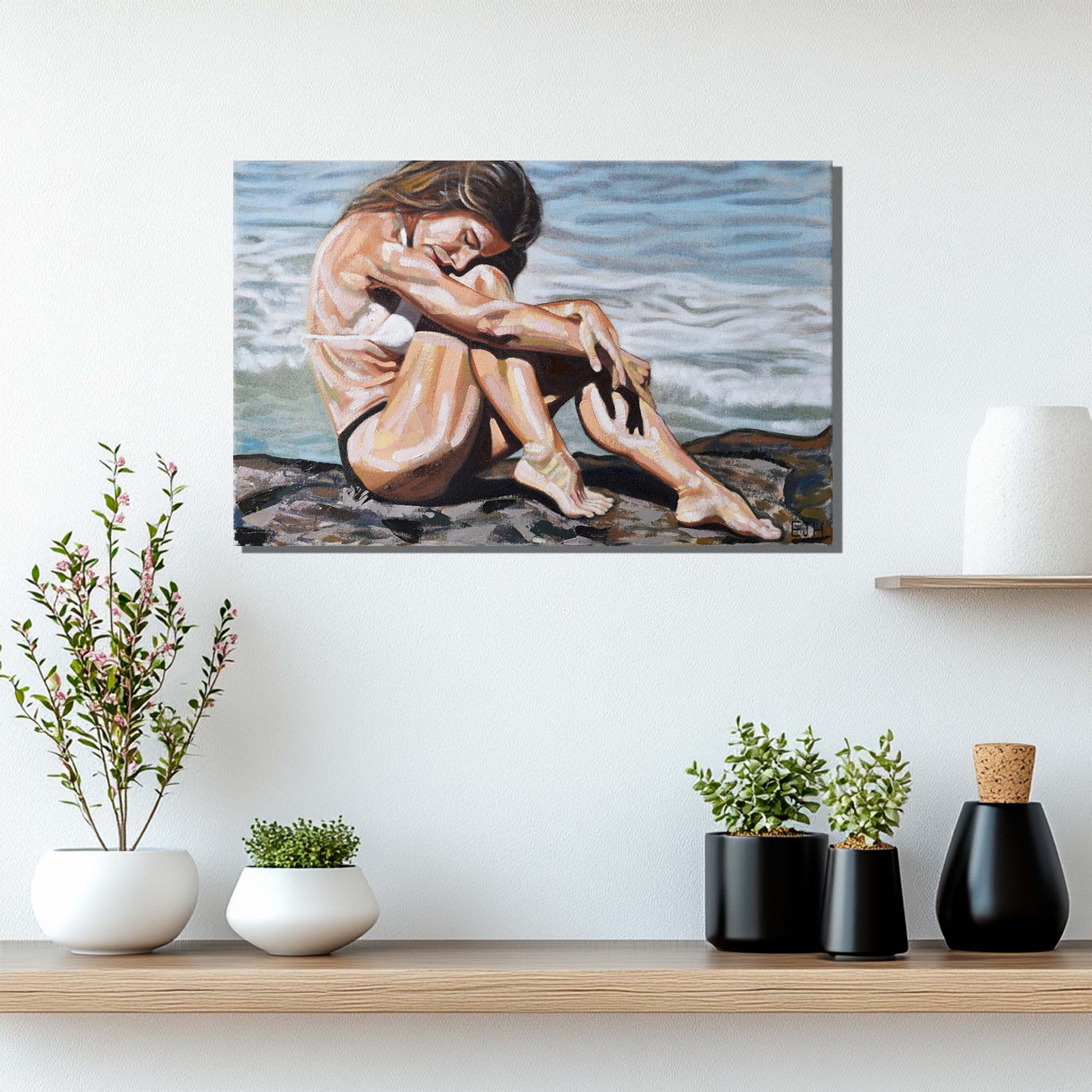 'Celestial Waves' oil painting of a woman sitting on a rock by the ocean hanging above a shelf with plants.