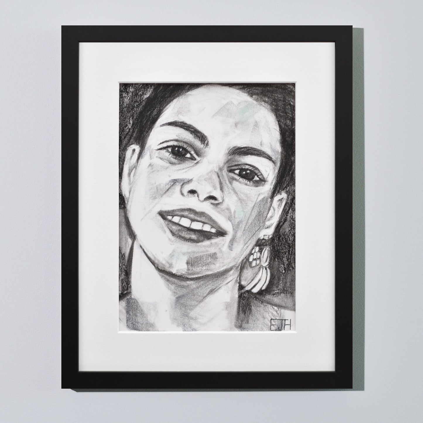 'Charisma' framed portrait drawing of a woman with a smile hanging on a neutral wall in the artist's studio.