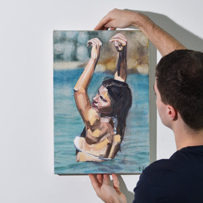Artist holding 'Follow The Sun' oil painting of a woman in the ocean against a blurry headland background.
