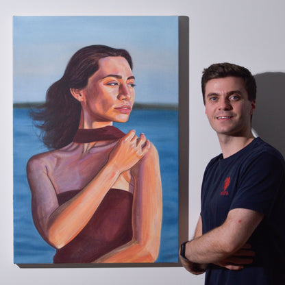 Artist standing next to 'Golden Hour' oil painting of a woman with a burgundy dress posing in Sydney harbor.