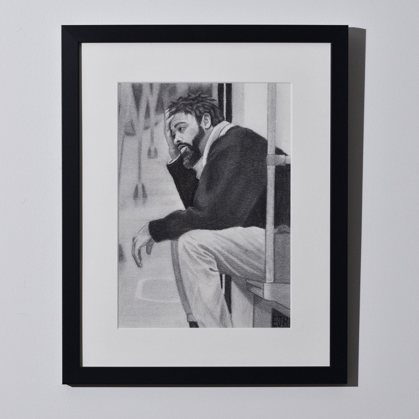 'Lost In My Head' framed portrait drawing of a man on metro seat hanging on a neutral wall in the artist's studio.