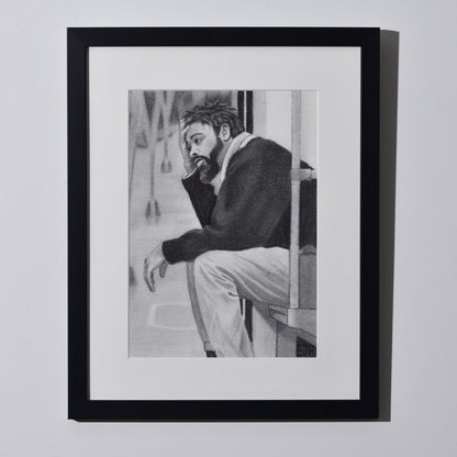 'Lost In My Head' framed portrait drawing of a man on metro seat hanging on a neutral wall in the artist's studio.