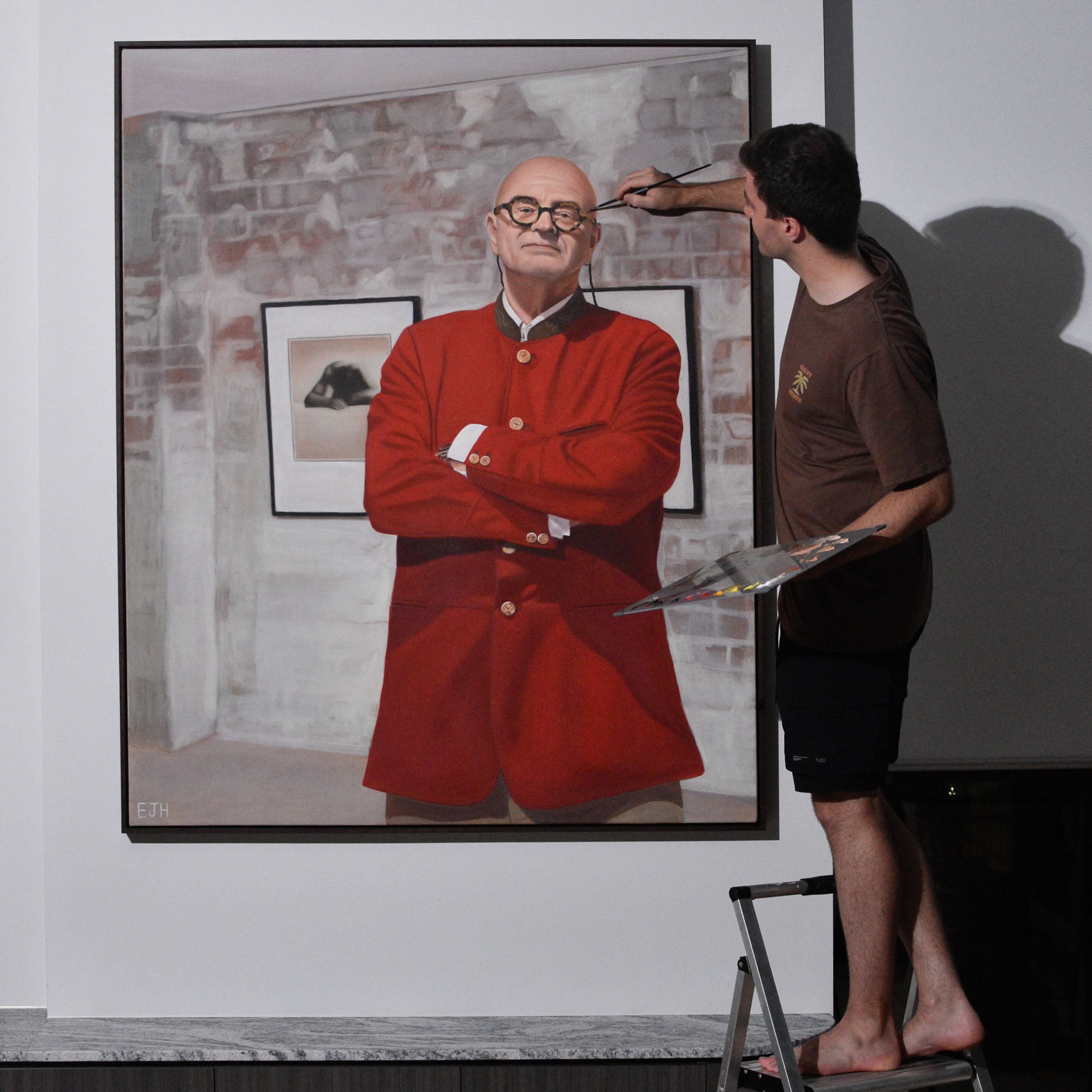 Artist painting 'Michael Reid OAM' a portrait of a man in a red coat.