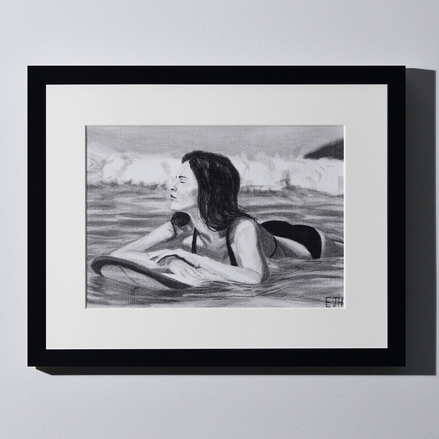 'Soul Surfer' framed portrait drawing of a woman in the ocean hanging on a neutral wall in the artist's studio.