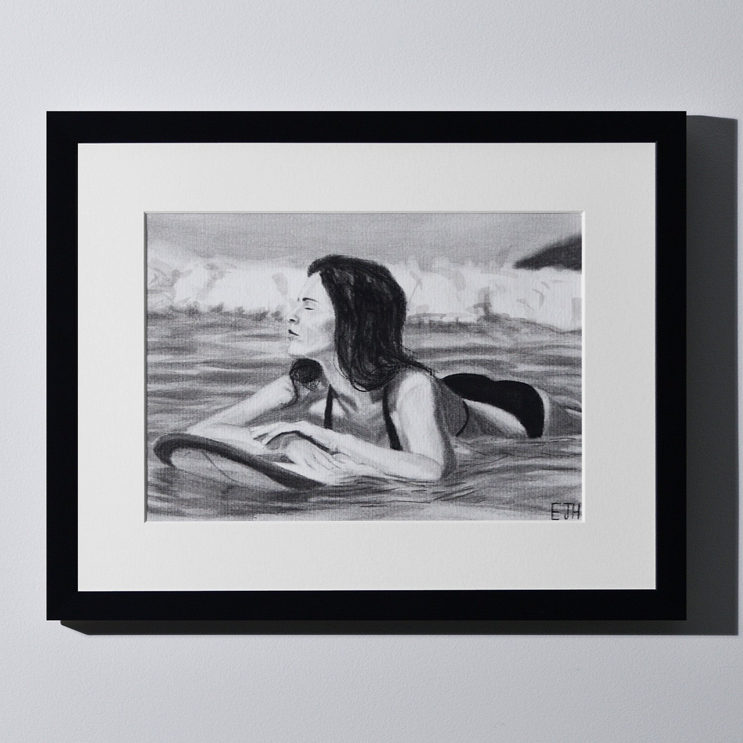 'Soul Surfer' framed portrait drawing of a woman in the ocean hanging on a neutral wall in the artist's studio.