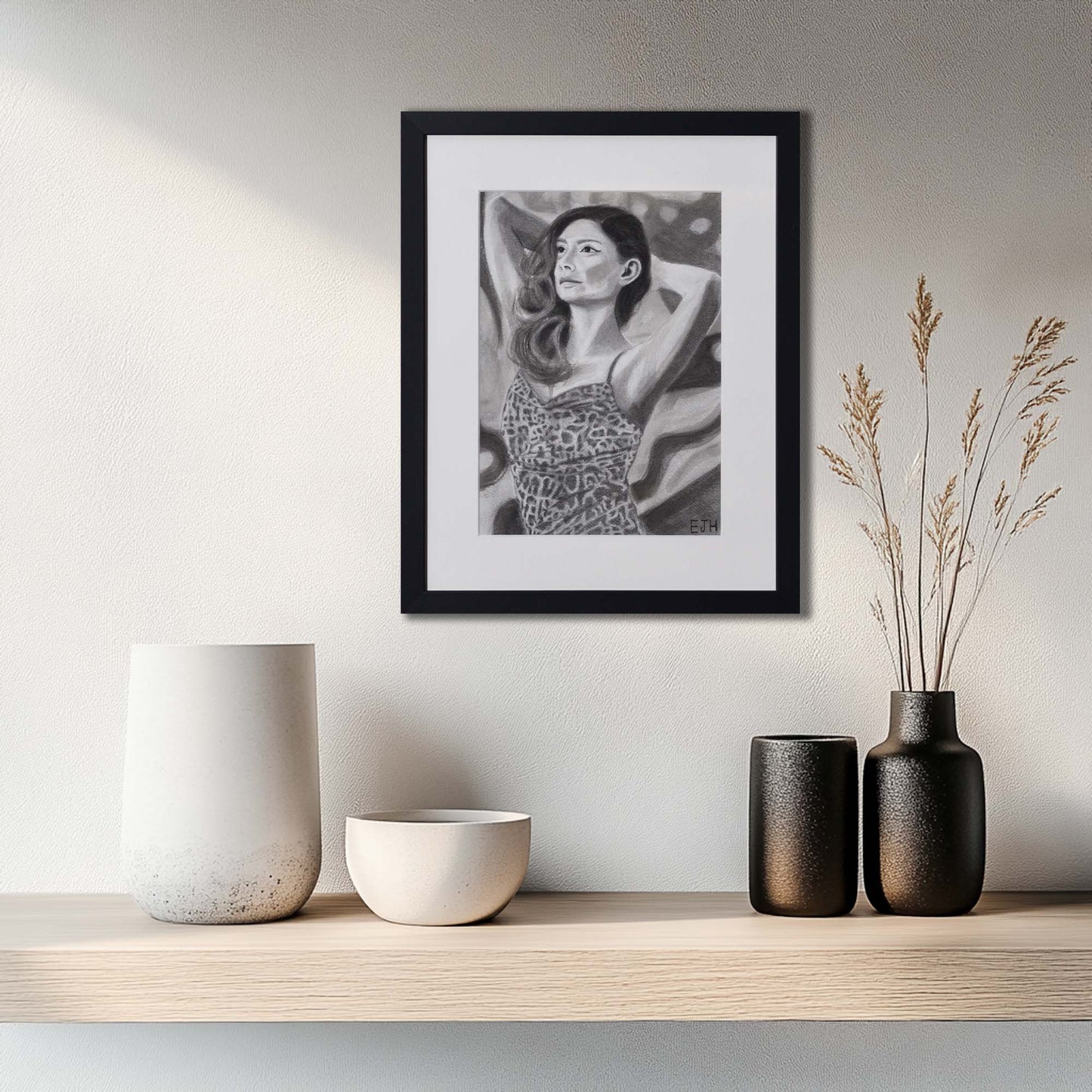 'The Spaces Between Patterns' framed portrait drawing hanging on a wall above a wooden shelf with decorative vases. 