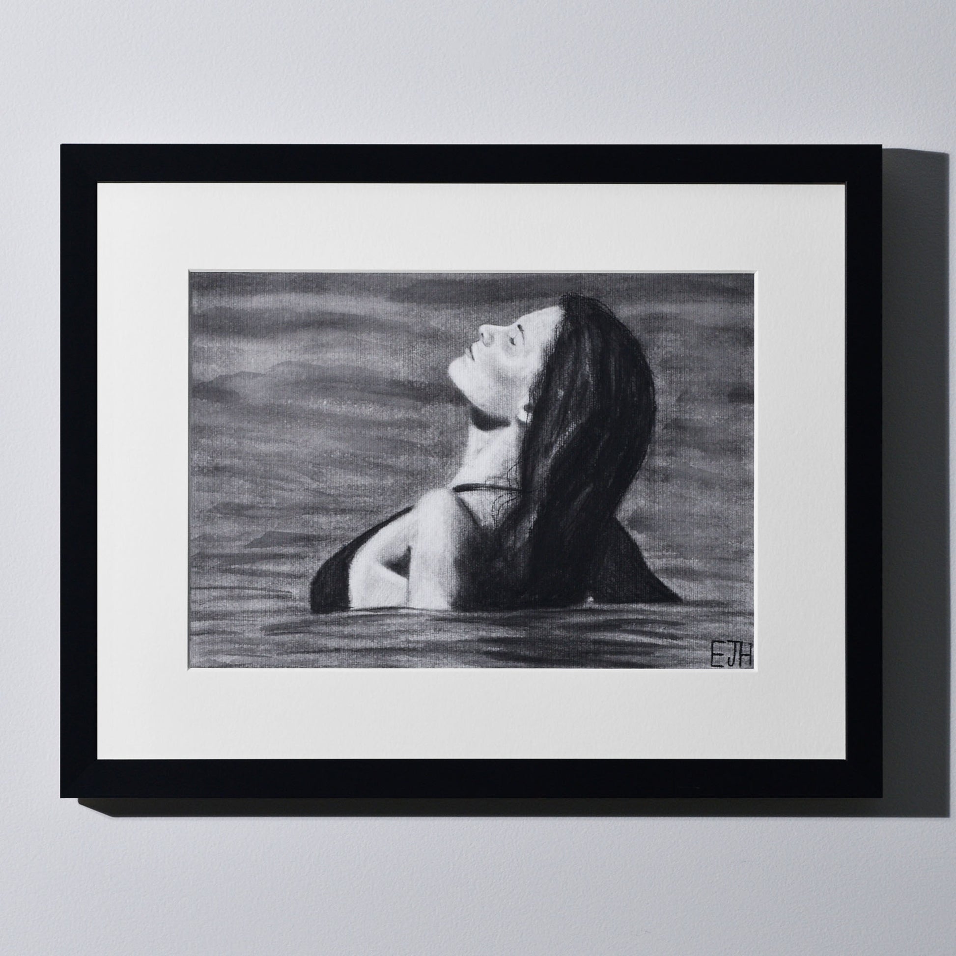 'The Sunbather' framed portrait drawing of a woman in the ocean hanging on a neutral wall in the artist's studio.