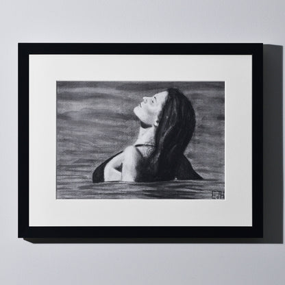 'The Sunbather' framed portrait drawing of a woman in the ocean hanging on a neutral wall in the artist's studio.