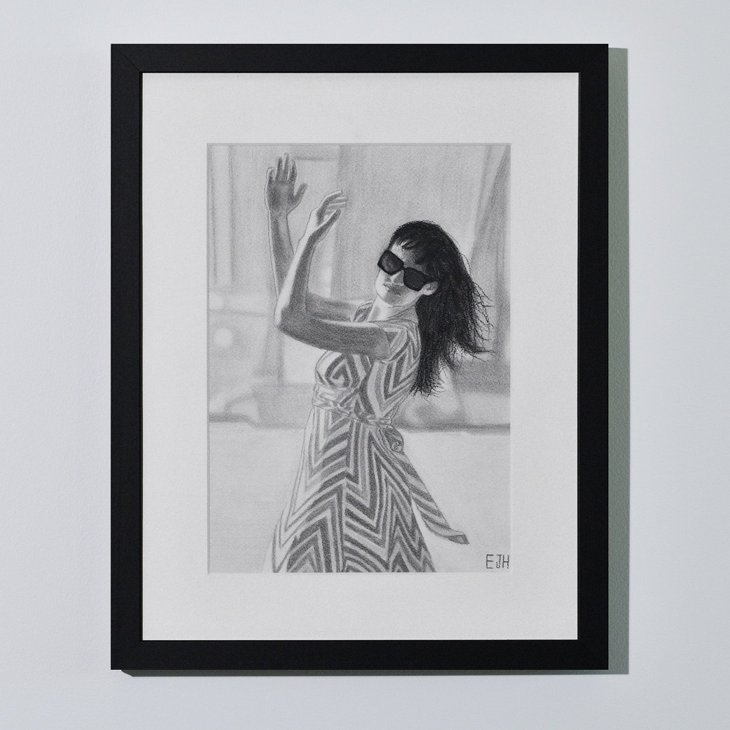 'When The World Prevails We Transform' framed portrait drawing of a woman in zigzag patterned dress hanging on a neutral wall in the artist's studio.