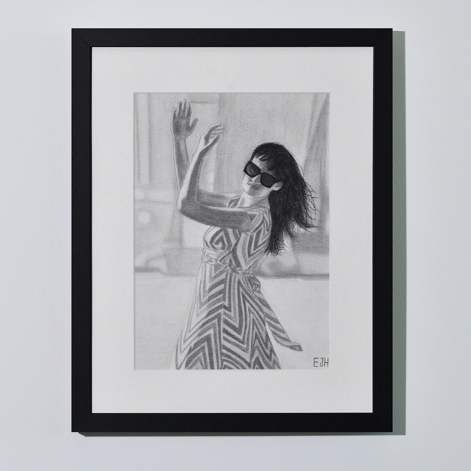 'When The World Prevails We Transform' framed portrait drawing of a woman in zigzag patterned dress hanging on a neutral wall in the artist's studio.