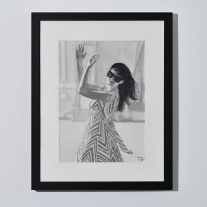 'When The World Prevails We Transform' framed portrait drawing of a woman in zigzag patterned dress hanging on a neutral wall in the artist's studio.