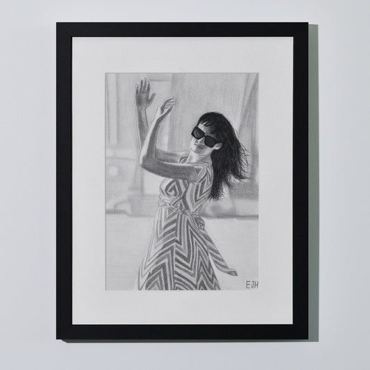 'When The World Prevails We Transform' framed portrait drawing of a woman in zigzag patterned dress hanging on a neutral wall in the artist's studio.