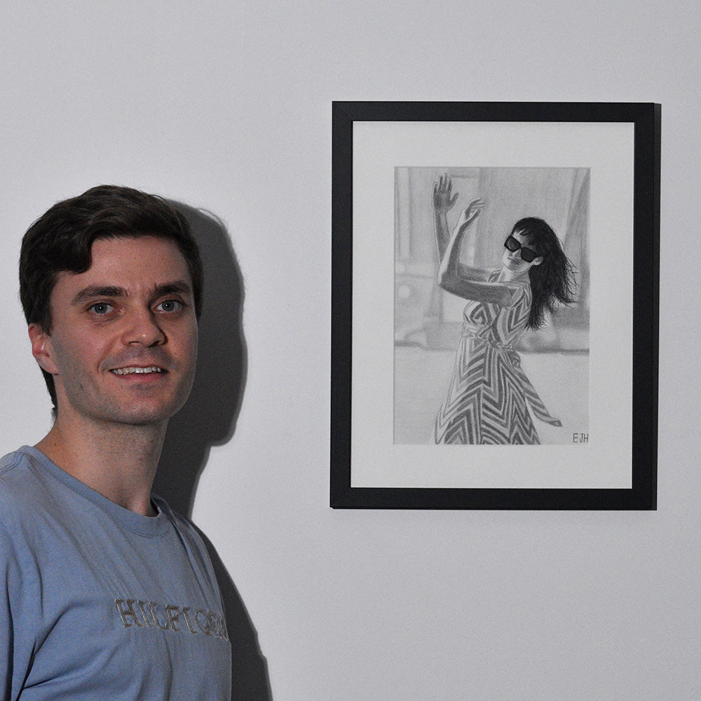 Artist standing next to 'When The World Prevails We Transform', framed drawing portrait on a wall.